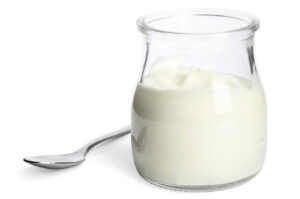 Gustoso yogurt bianco in vaso di vetro e cucchiaio su sfondo bianco