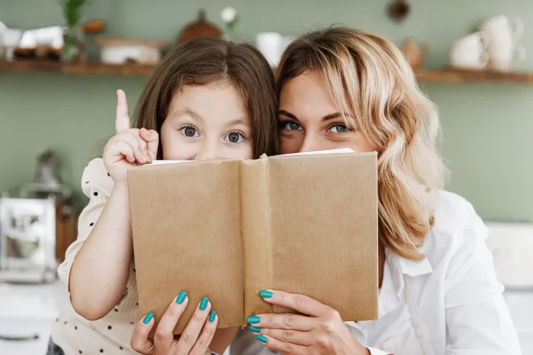 Madre e aiutante figlia in cucin che si nascondono dietro un libro di ricette